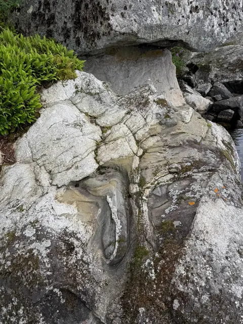 Folded and banded bedrock beneath a boulder at the water's edge