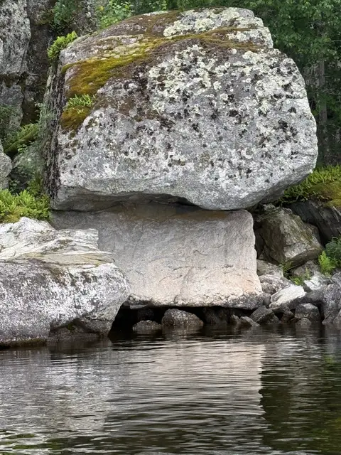 Glacial erratic boulder perched on bedrock above the water