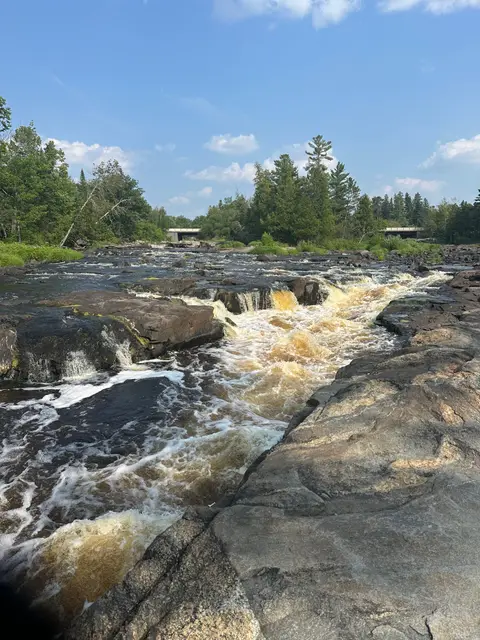 Whitewater sheeting across a broad granite shelf under blue sky