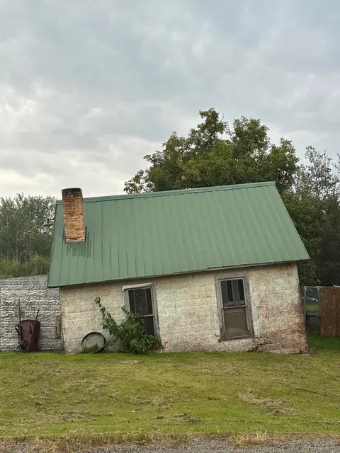 Old masonry cabin with a green metal roof and brick chimney